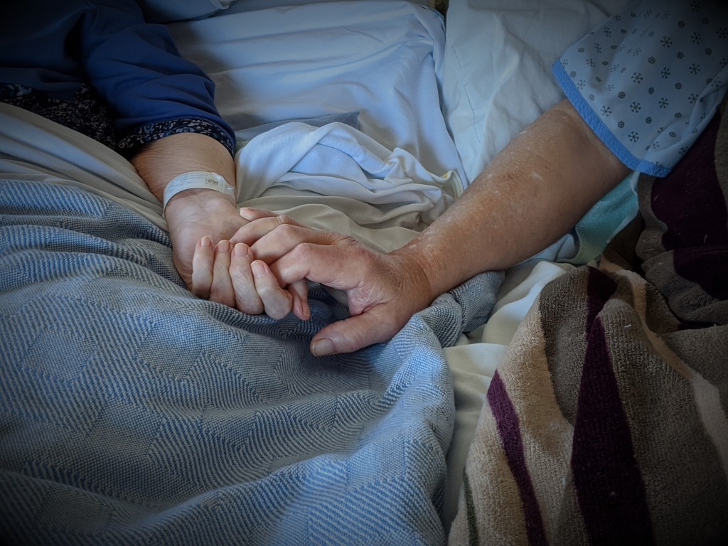 photo of my mom and dad holding hands in the hospital beds at the care home 